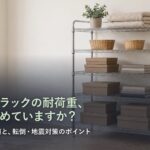 明るい部屋の壁際に置かれた5段のスチールラック。下段に重い物、上段に軽い物が並んでいる。「スチールラックの耐荷重、正しく読めていますか？ 棚板ごとの数値と、転倒・地震対策のポイント」の文字入り